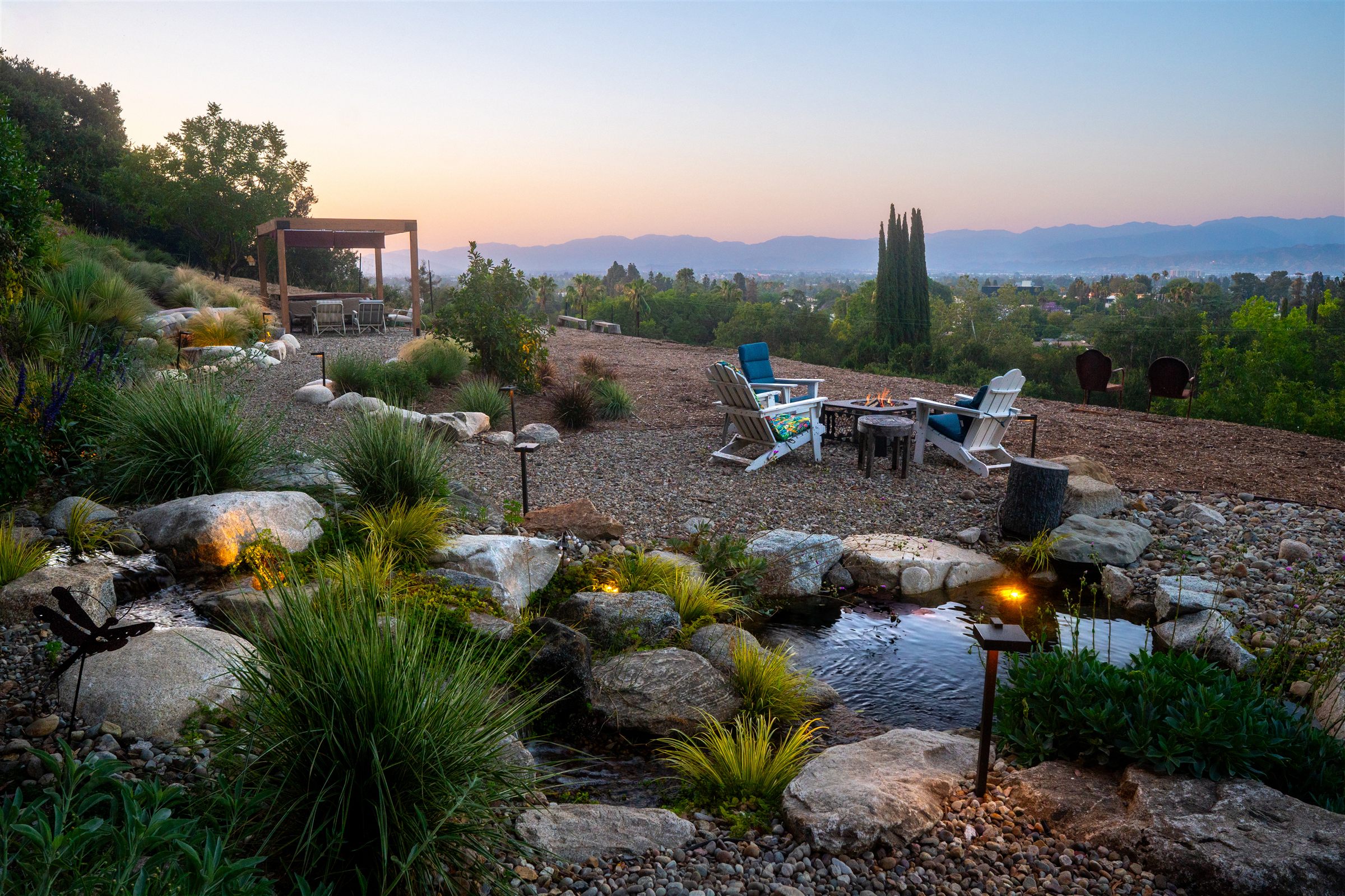 Hillside backyard fire pit seating area with a custom water feature and mountain view at dusk