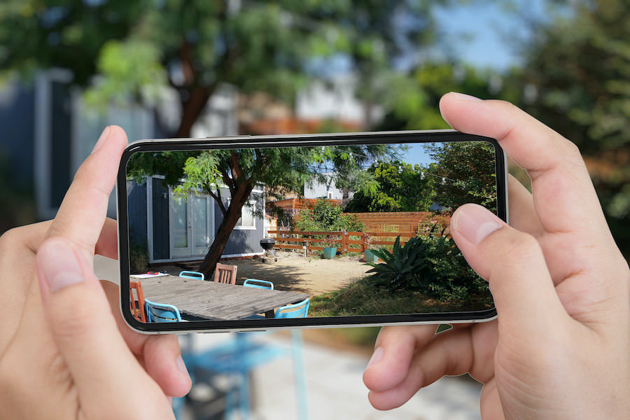 A homeowner photographing their own backyard on a phone to send to their YardMap designer