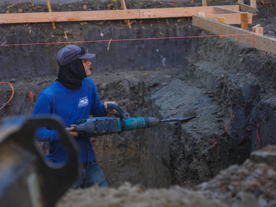 Crew member using a jackhammer to break ground during construction