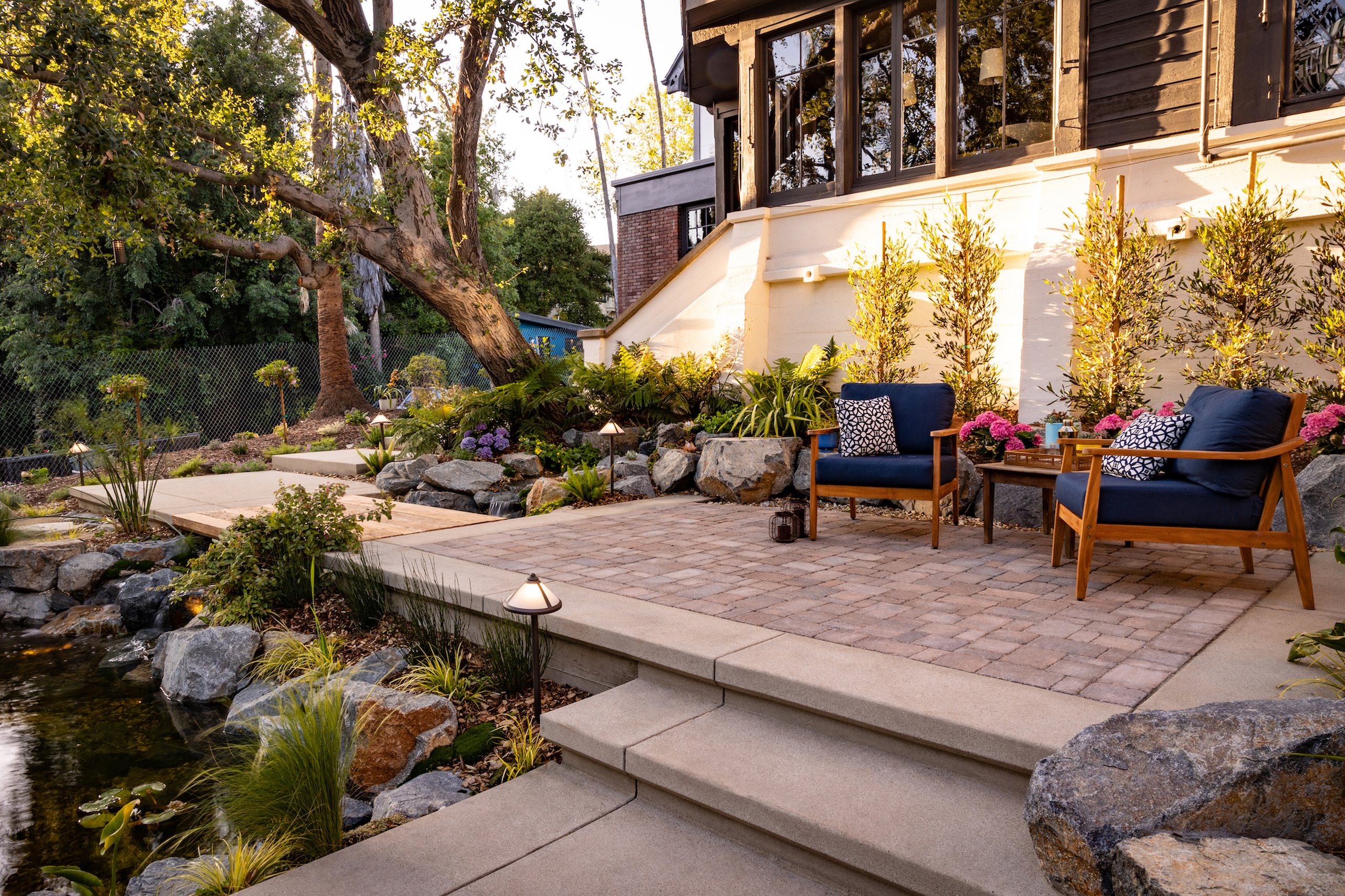 A patio with natural stone work and seating area nestled under a mature oak tree with layered landscape lighting