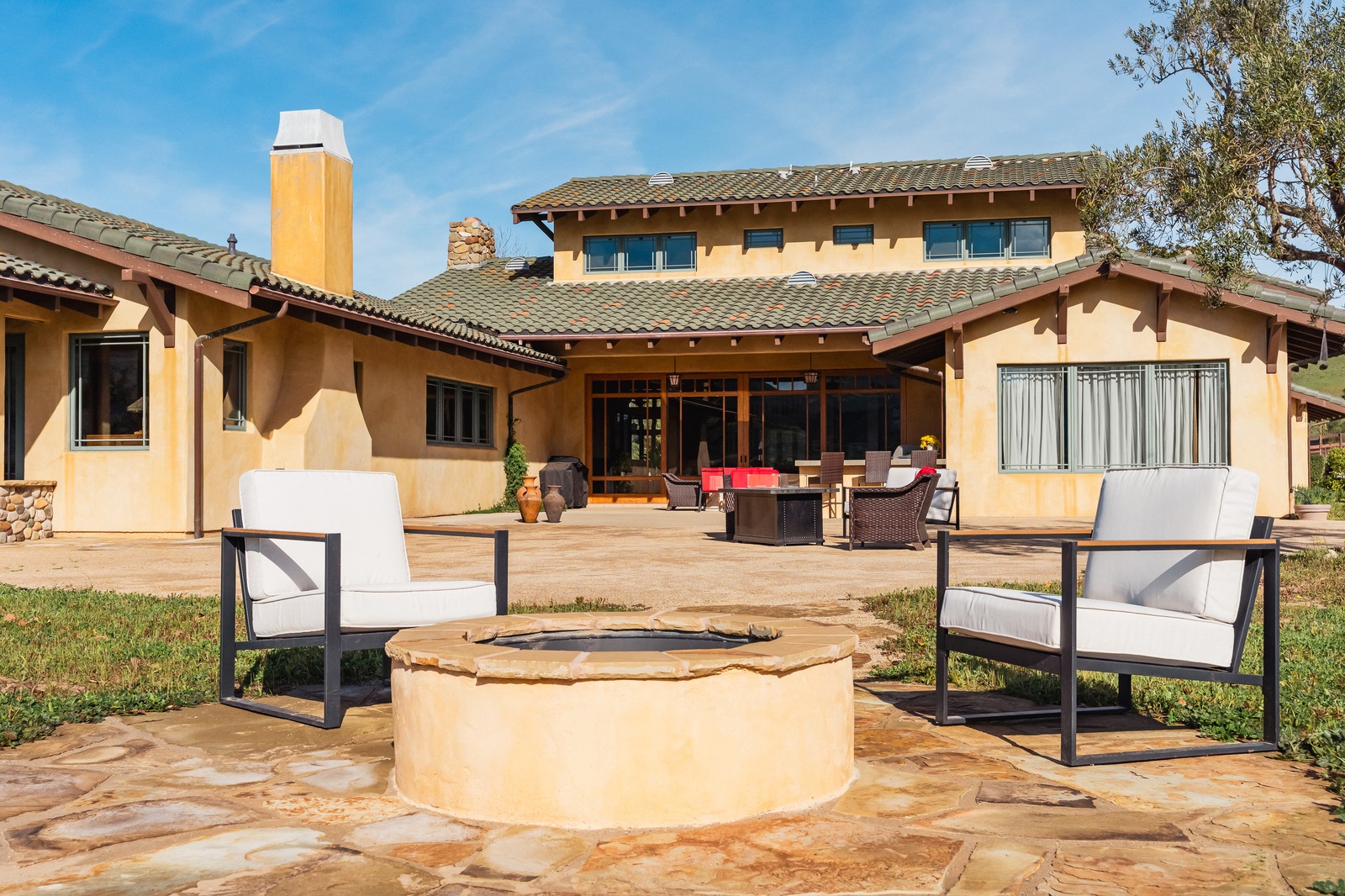 Finished stucco gas fire pit ringed by flagstone paving with two cushioned chairs facing the house