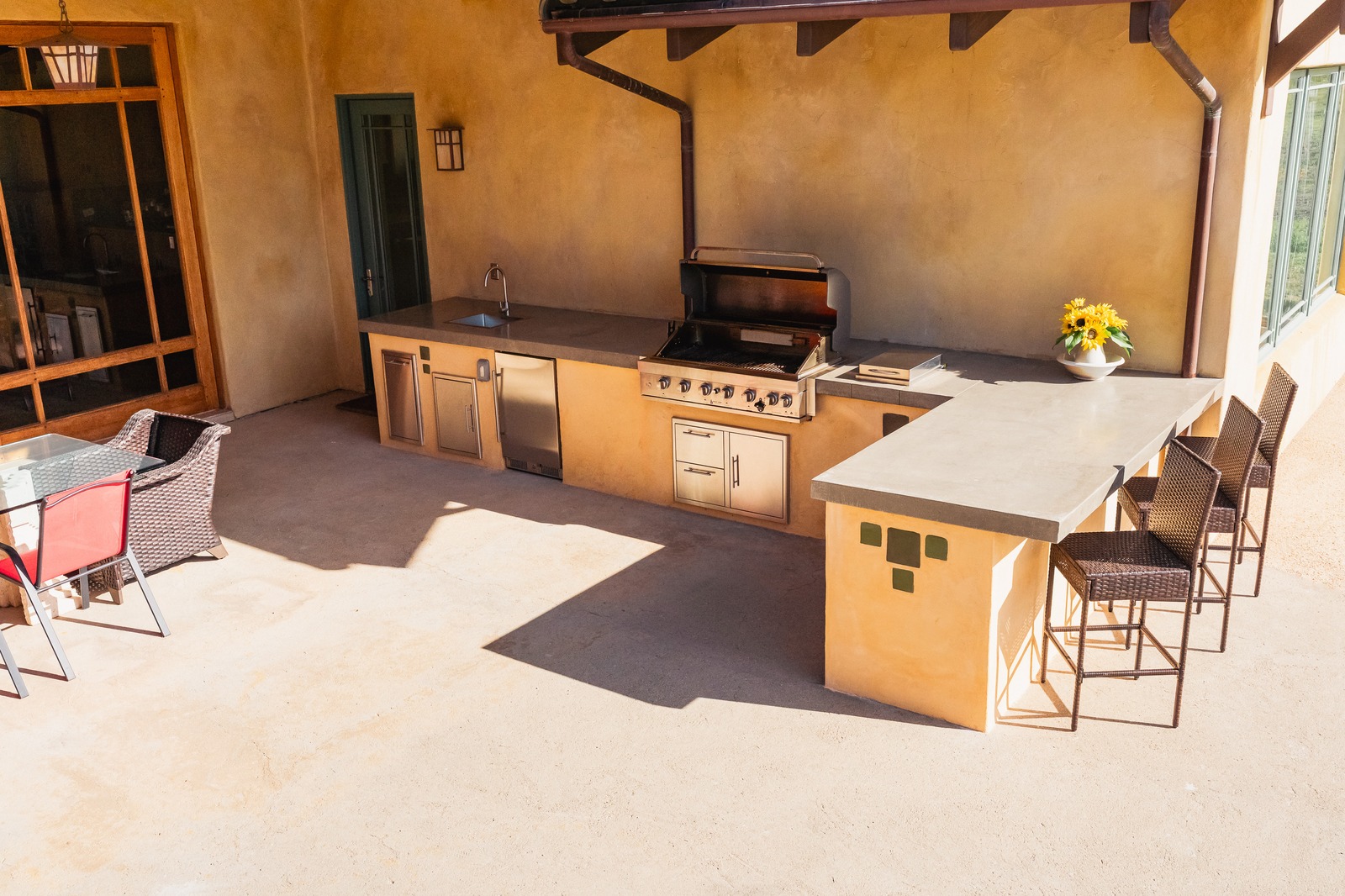 Covered patio outdoor kitchen with concrete counters, a stainless grill, and a seating bar with woven barstools