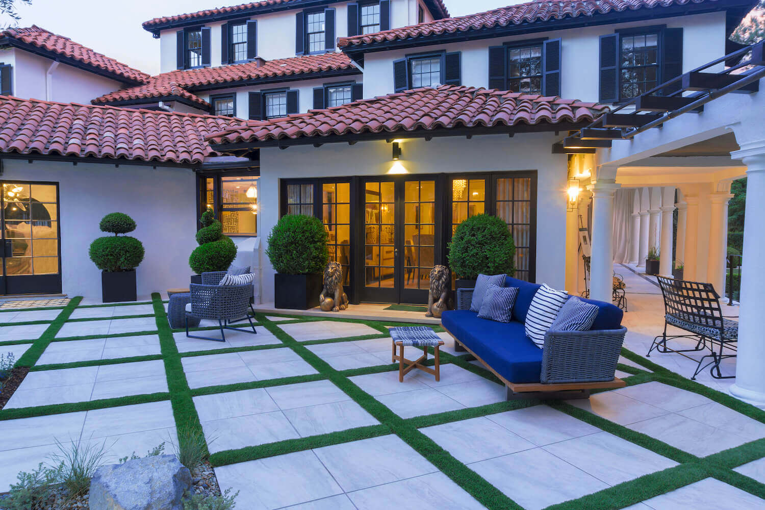 Large-format light stone pavers set in a turf grid pattern in a courtyard with a blue outdoor sofa and Spanish Colonial architecture