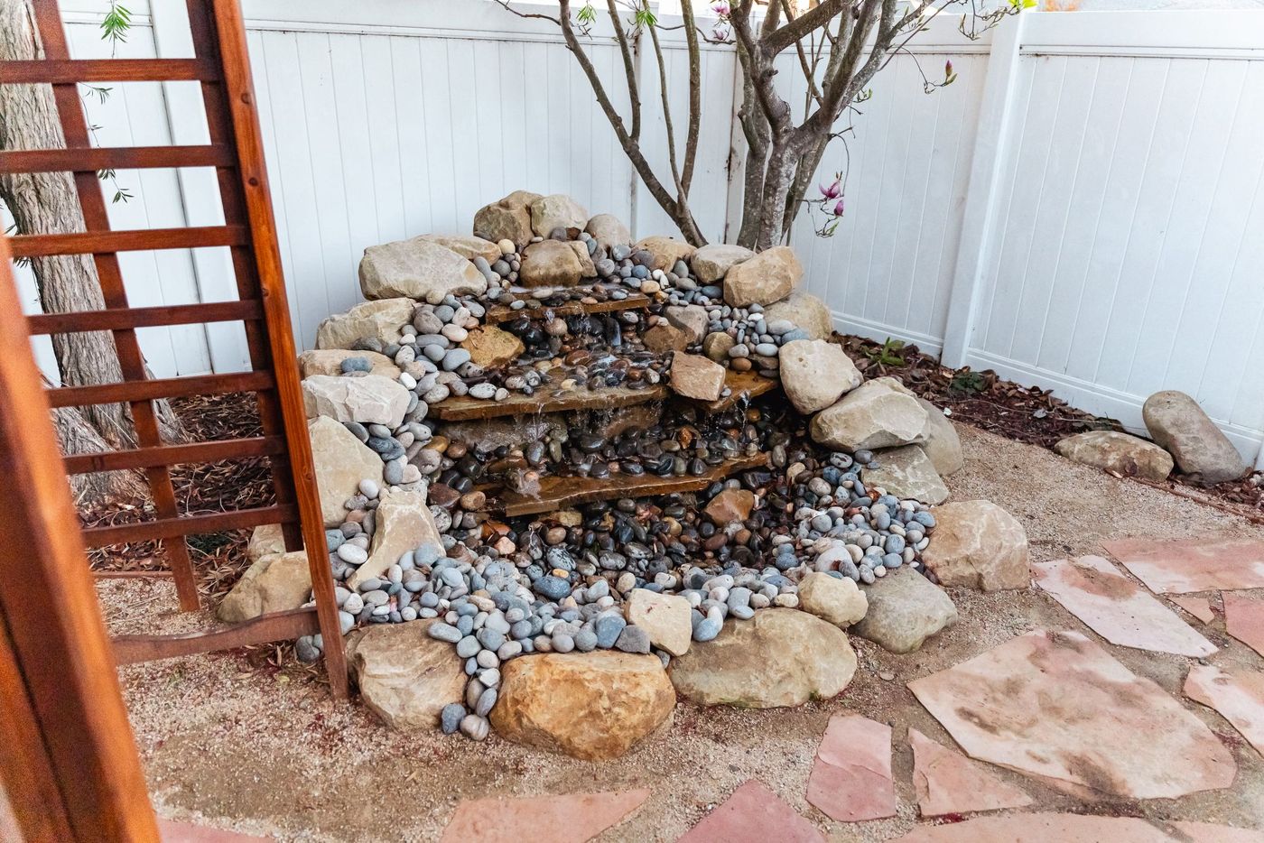 Close-up of tiered natural stone waterfall surrounded by river rock in a backyard patio setting.