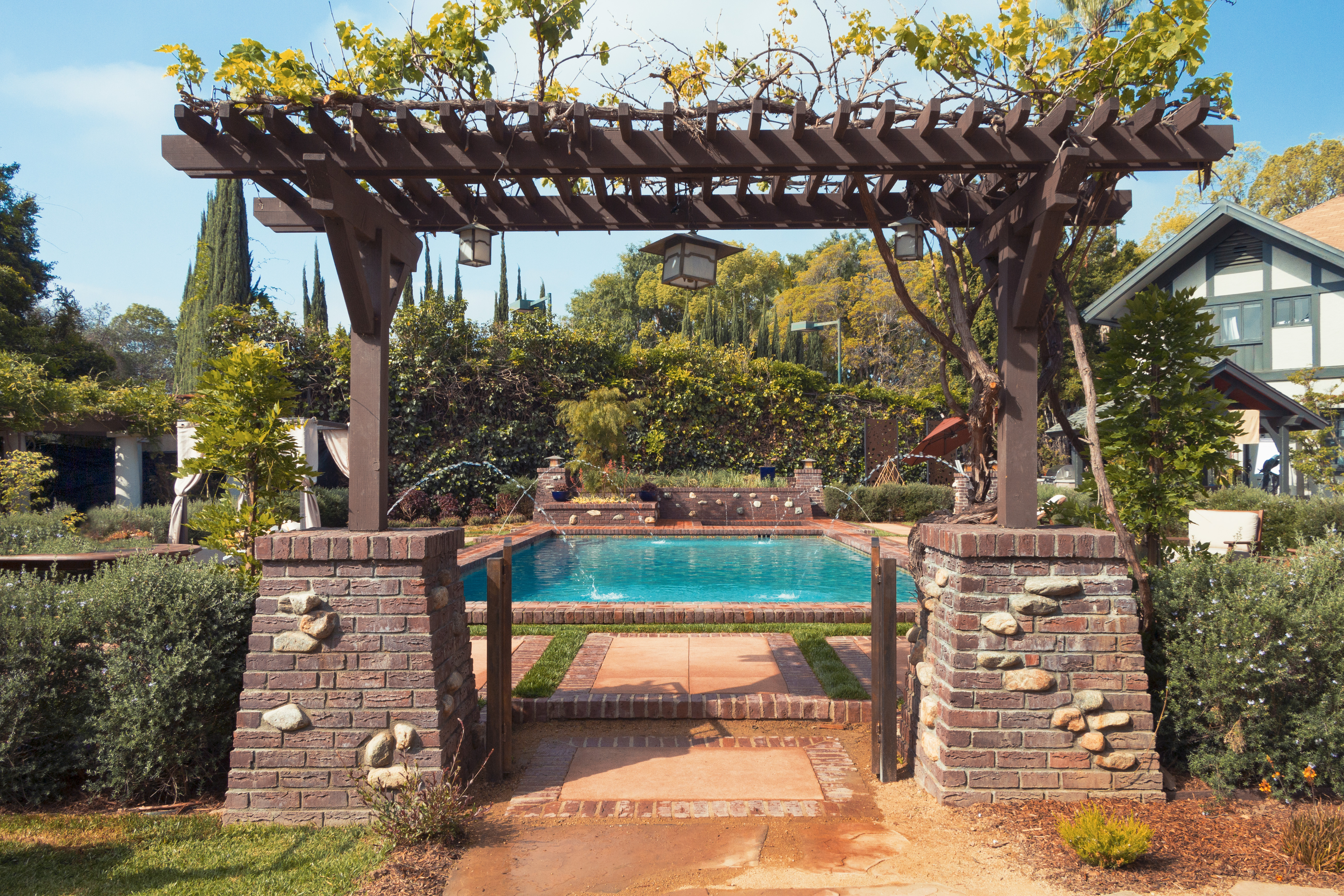 A wood pergola creating an outdoor room that connects the lawn to a lounge seating area with planting and hillside beyond