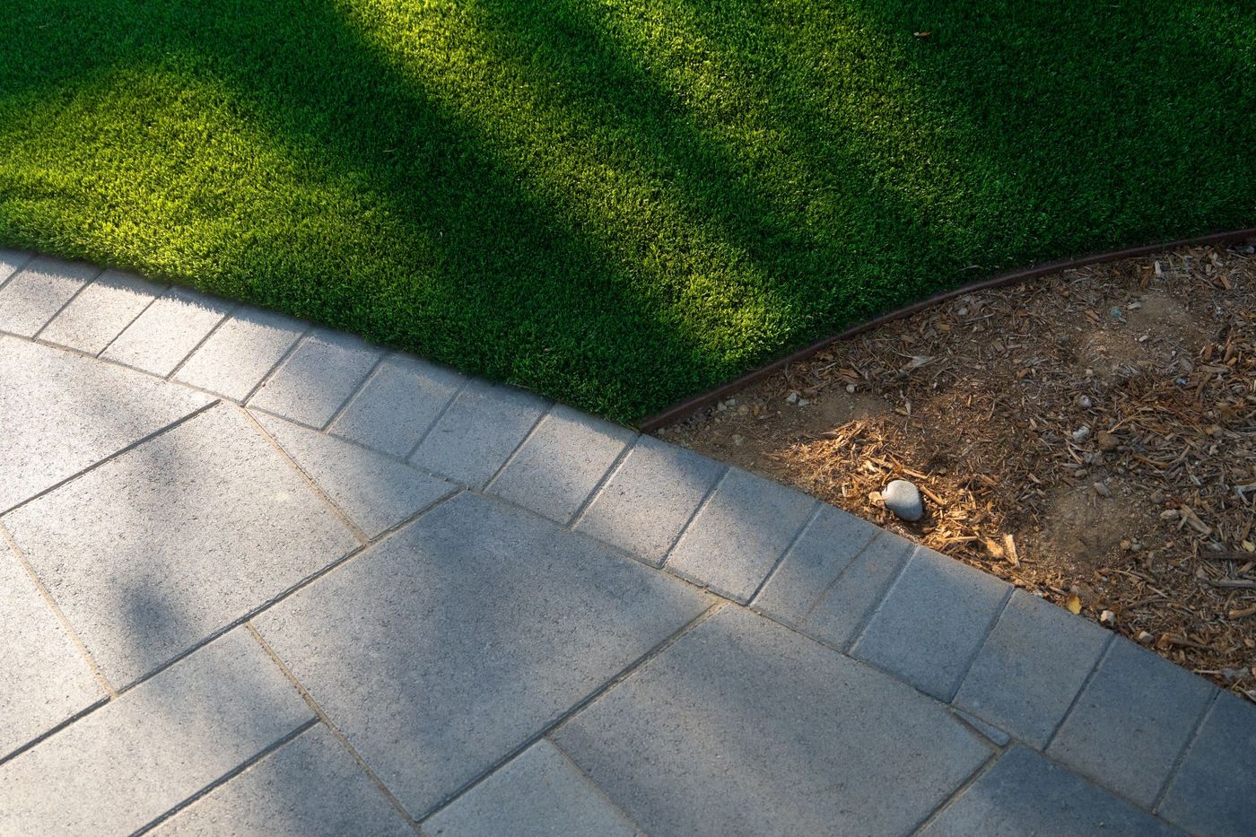 Close-up of synthetic turf meeting geometric concrete pavers and mulch planting bed, showing clean edging detail in a contemporary California landscape.
