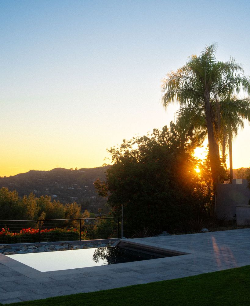 Modern square spa beside palm trees and hillside landscape during warm sunset lighting.