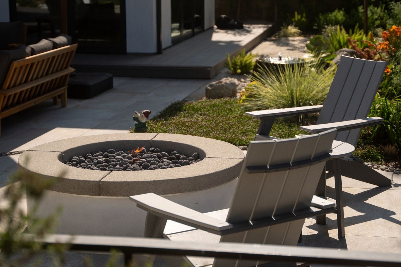 A round fire pit with river-rock filler beside modern adirondack chairs and a succulent garden