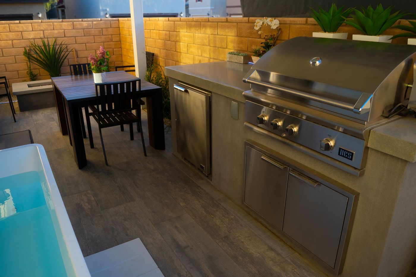 Modern small-space outdoor kitchen featuring stainless steel grill, integrated storage, and concrete counter adjacent to plunge pool.