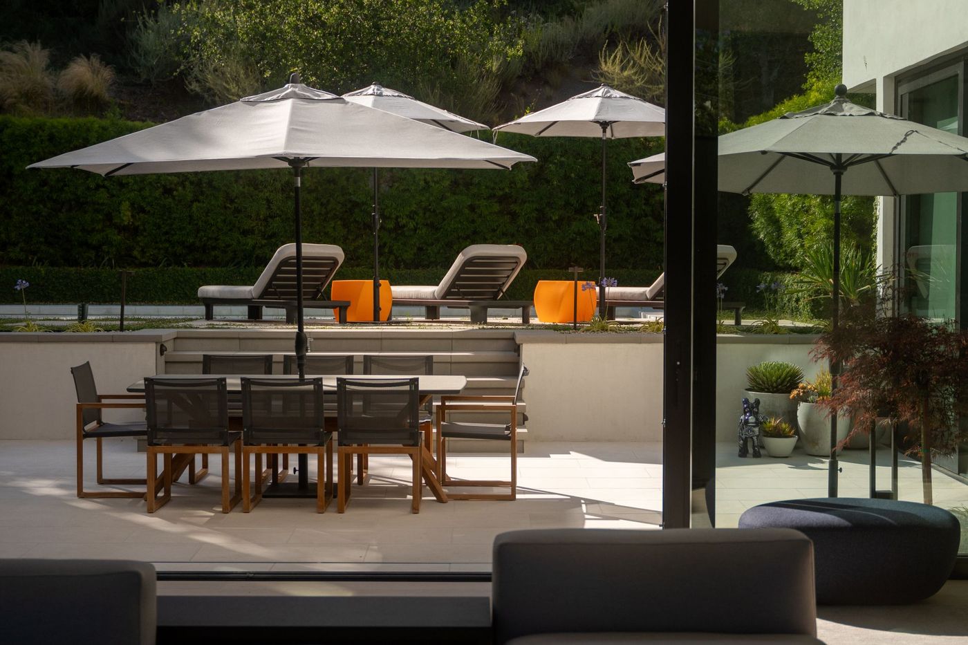 Shaded outdoor dining patio with table and chairs overlooking a landscaped backyard and pool lounge area