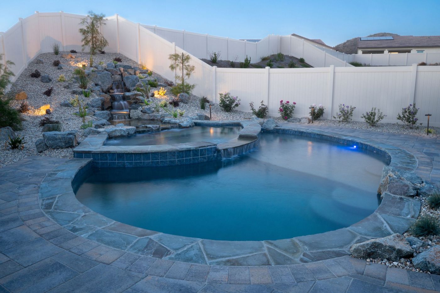 A freeform lagoon pool with a natural rock waterfall lit at dusk