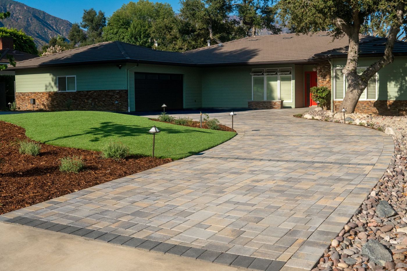 Residential front yard featuring curved paver driveway, green turf lawn, landscape lighting, and modern home facade in a California design-build project.