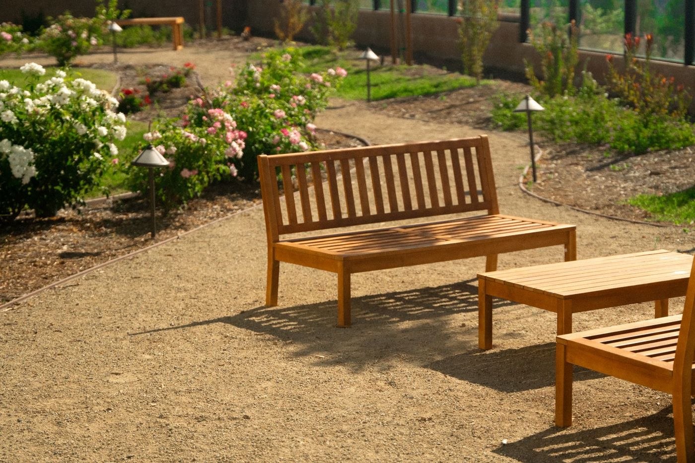 Wood bench seating beside blooming flower beds and winding decomposed granite walkway in a serene residential courtyard landscape.