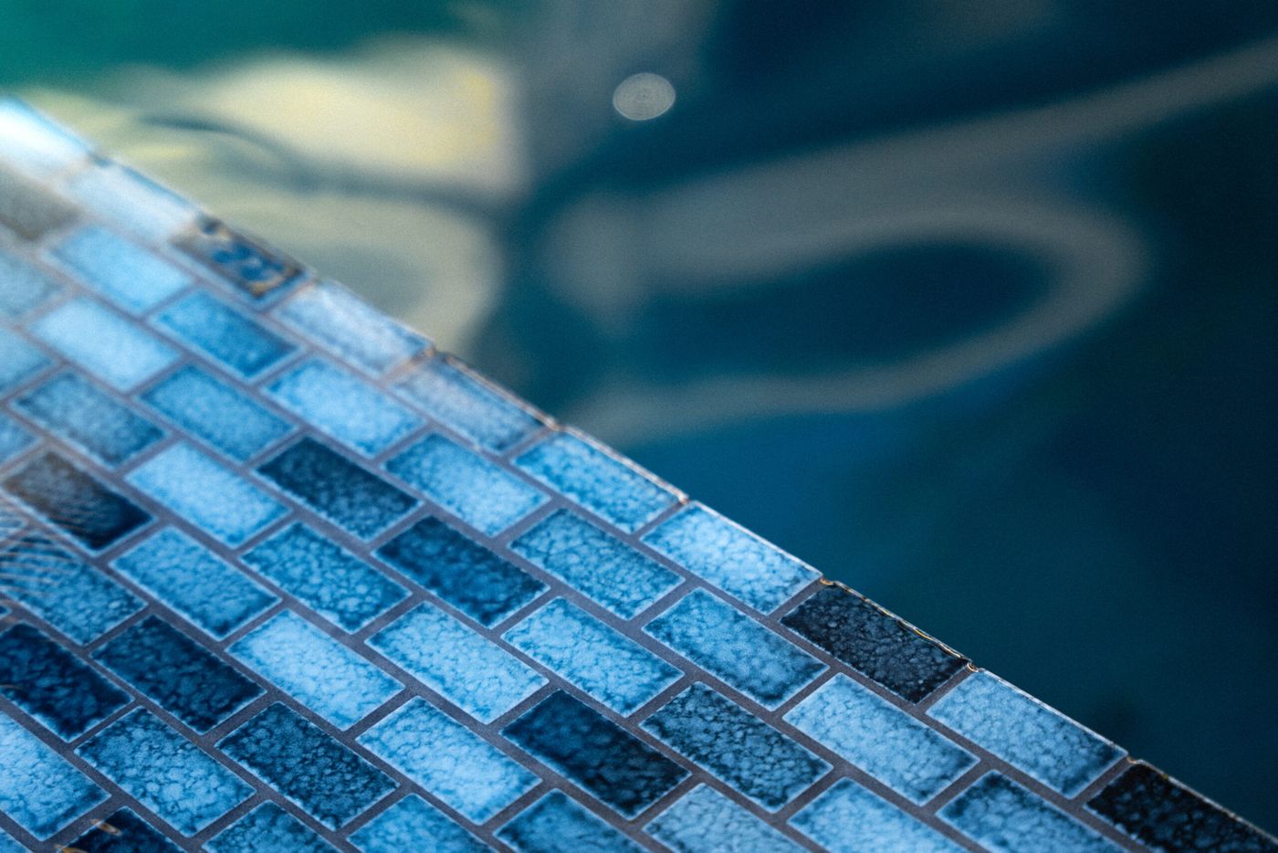 Detailed view of blue glass tile pool coping and water surface in a contemporary backyard swimming pool.