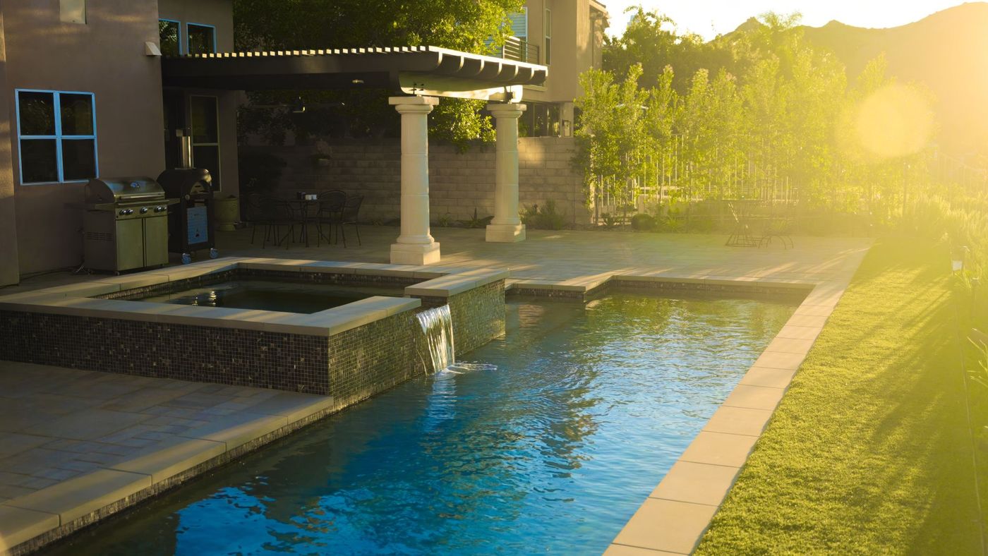 Contemporary lap pool featuring raised spa, waterfall, covered pergola patio, and landscaped yard.