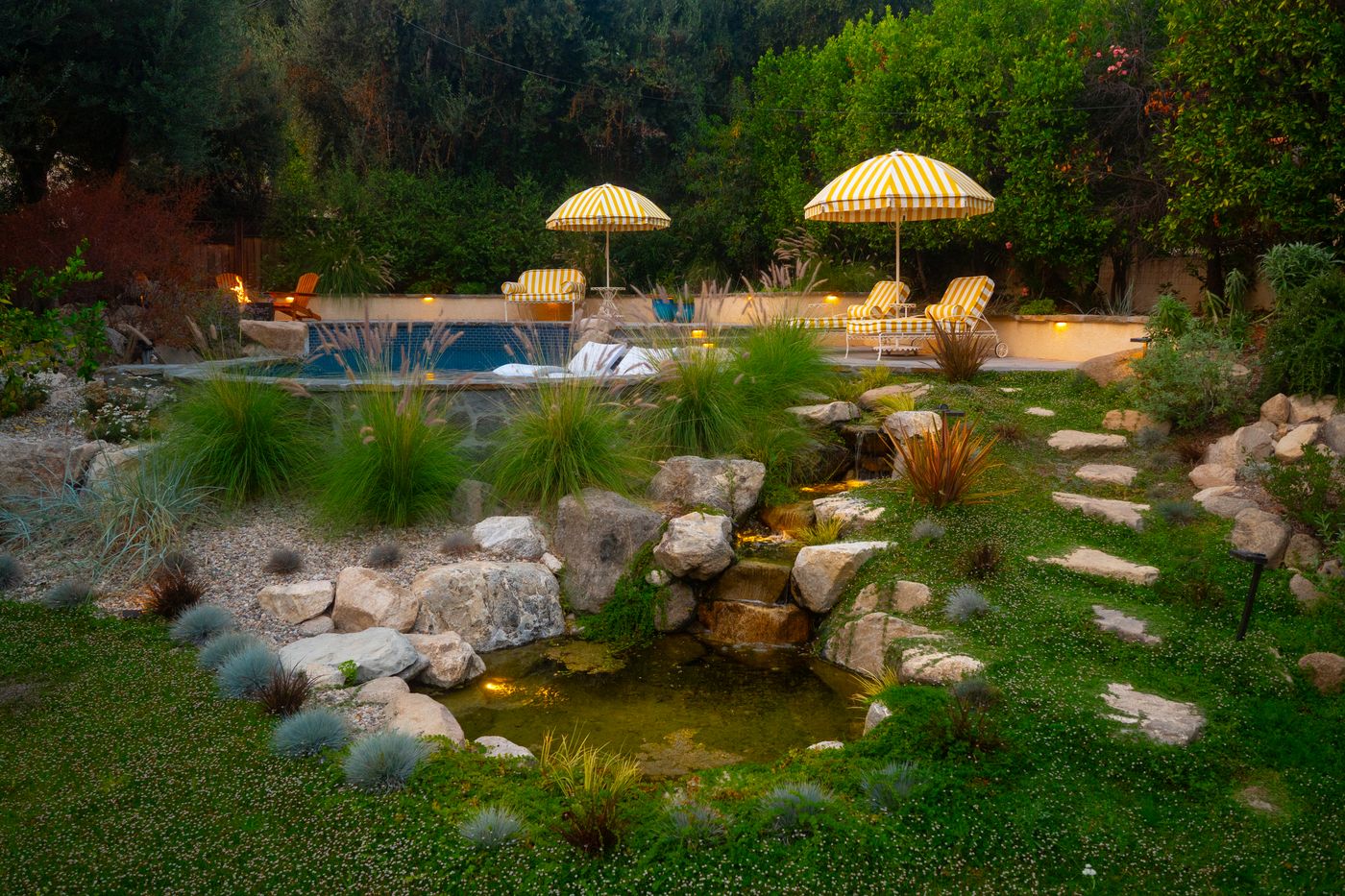 A large recreational water garden with a swimming area, pond, boulders, and lush planting