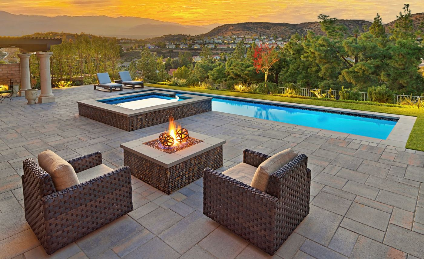Modern swimming pool with spa, fire pit seating area, and panoramic sunset hillside view in a luxury backyard.