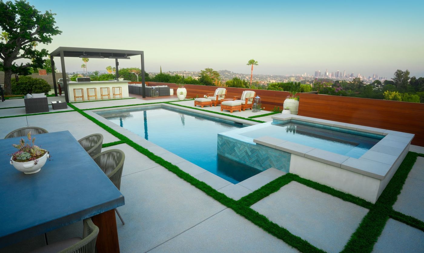 A modern rectangular pool with a raised spa, tiled edge and an outdoor kitchen behind it