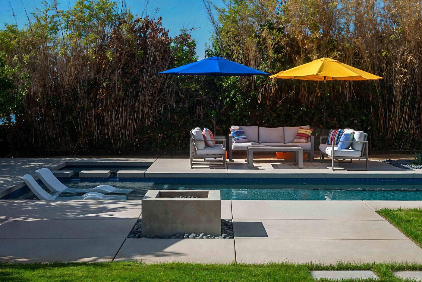 Contemporary swimming pool with tanning ledge, fire feature, and outdoor seating area in a landscaped backyard.