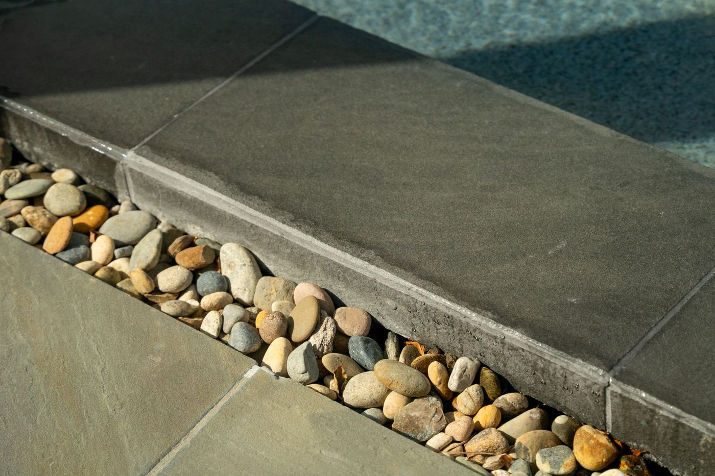 Close view of smooth dark pool coping beside natural river rock drainage channel highlighting clean minimalist pool design detail.