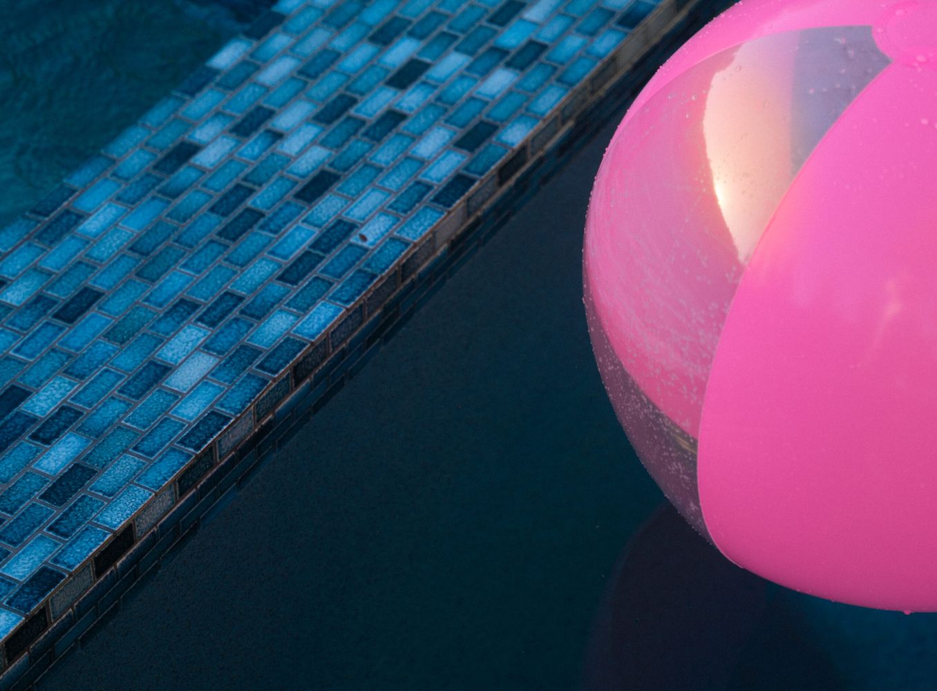Close-up of blue glass pool tile edge with a pink inflatable pool float in clear swimming pool water.