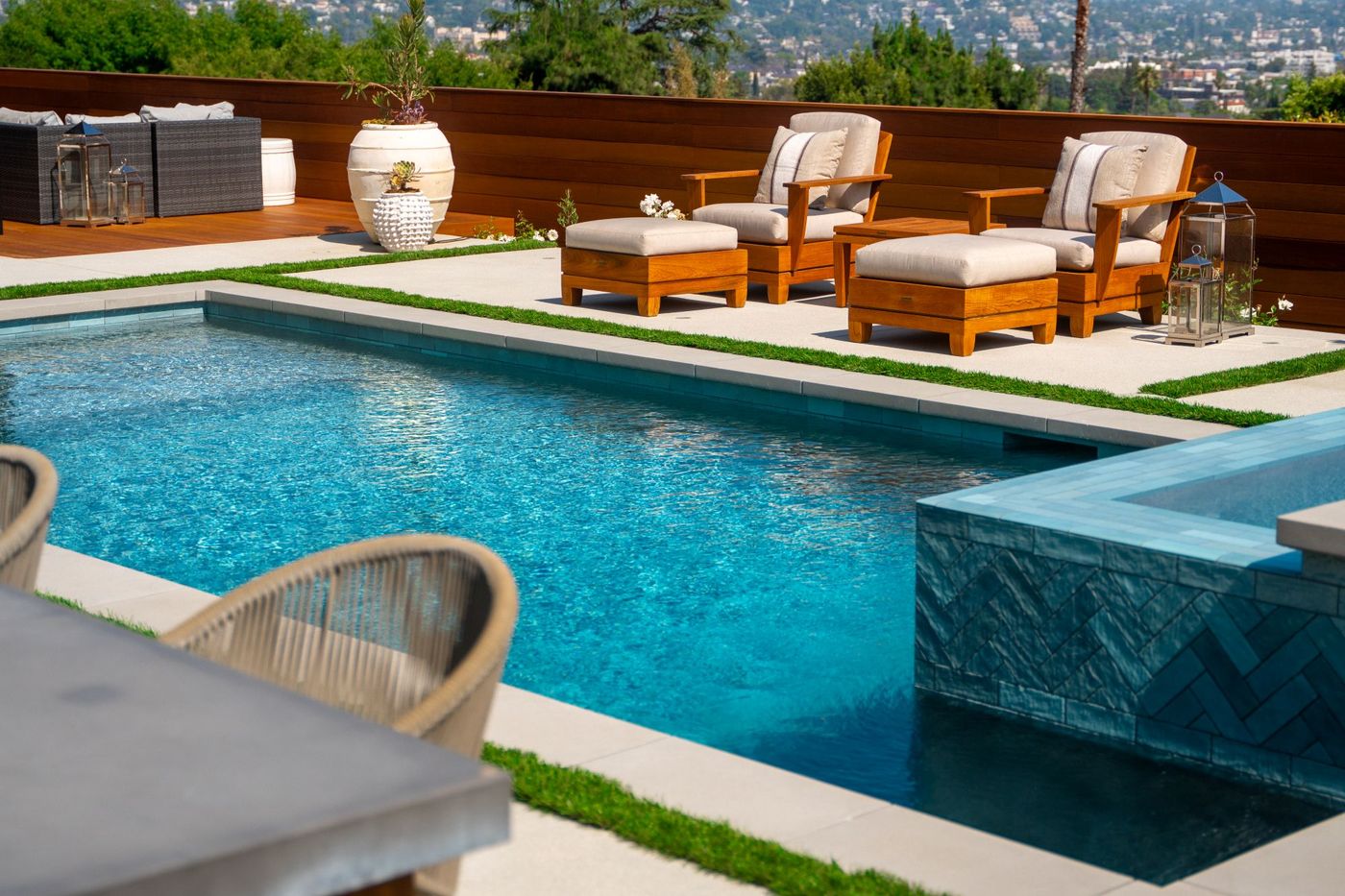 Clear blue swimming pool water beside contemporary patio seating, decorative planters, and clean-lined landscape design.
