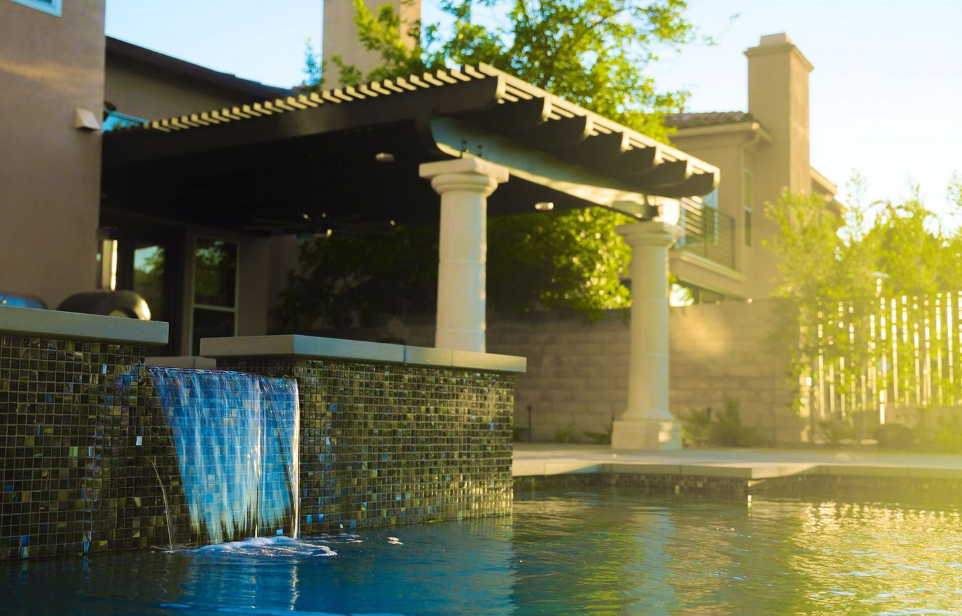 Contemporary lap pool featuring raised spa, waterfall, covered pergola patio, and landscaped yard.