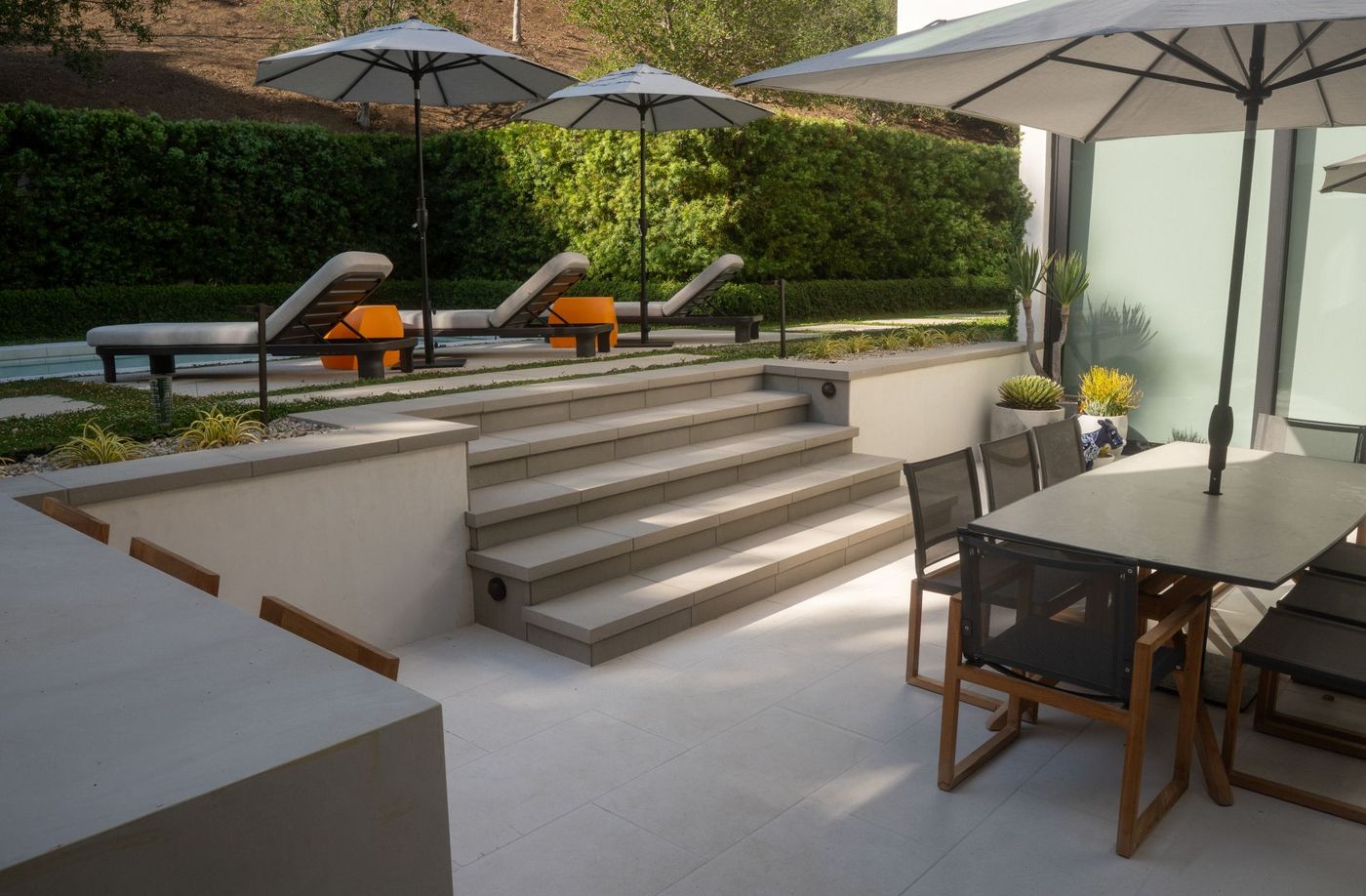 Concrete steps leading from patio dining space to pool lounge area surrounded by manicured landscape