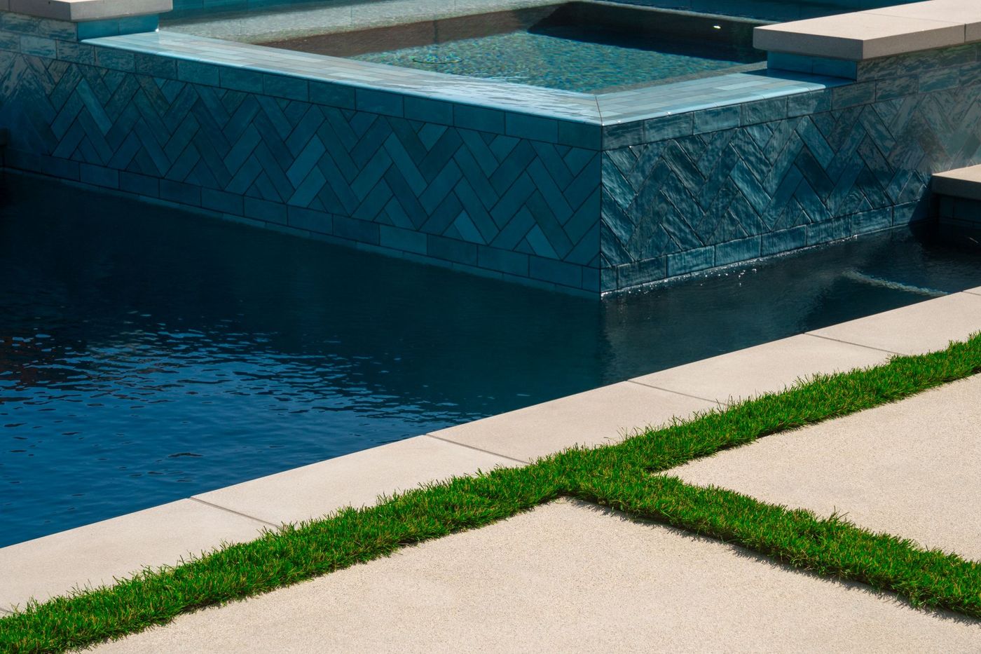 Contemporary raised spa with blue herringbone tile facing, clean concrete coping, and adjacent swimming pool waterline detail.