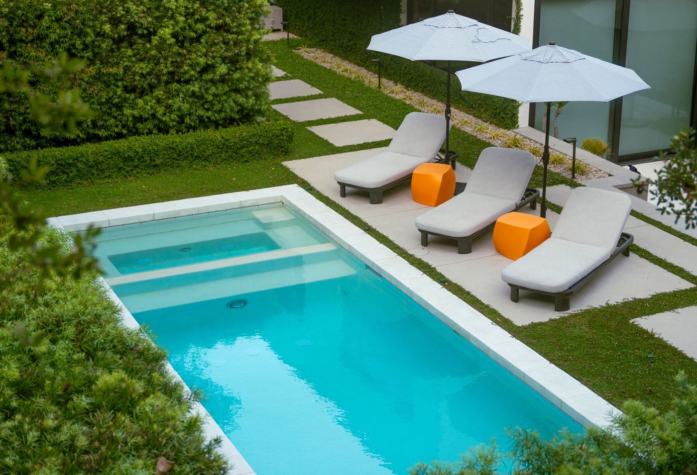 Overhead perspective of turquoise rectangular pool with cushioned lounge chairs and geometric stepping stones