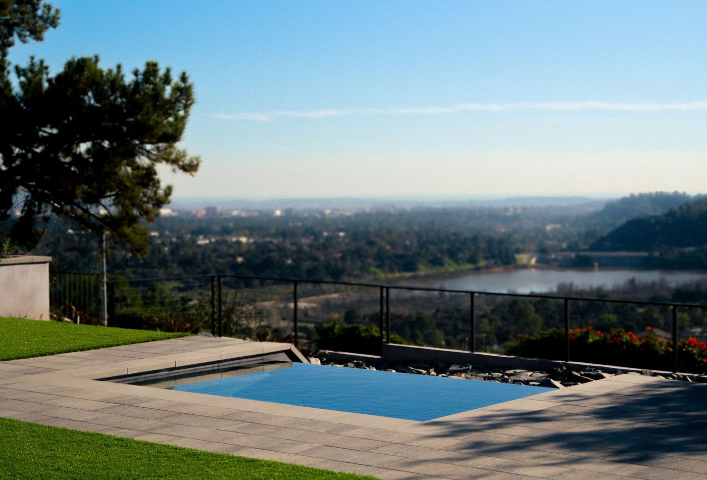 Square backyard spa overlooking lake, trees, and distant skyline in a contemporary landscape design.