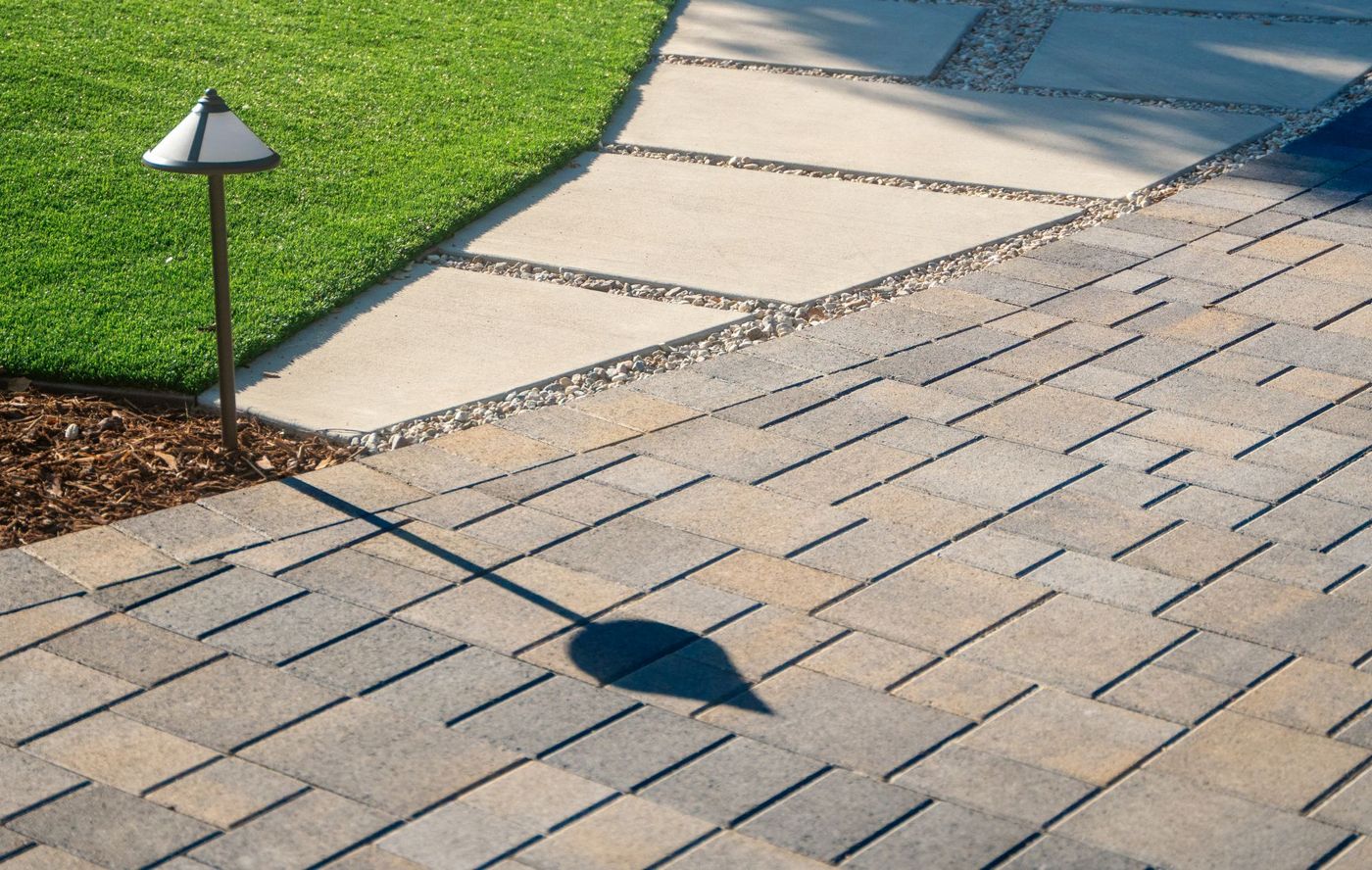 Concrete stepping stone path bordered by gravel joints and adjacent paver driveway, highlighting clean geometric hardscape design in a contemporary landscape.