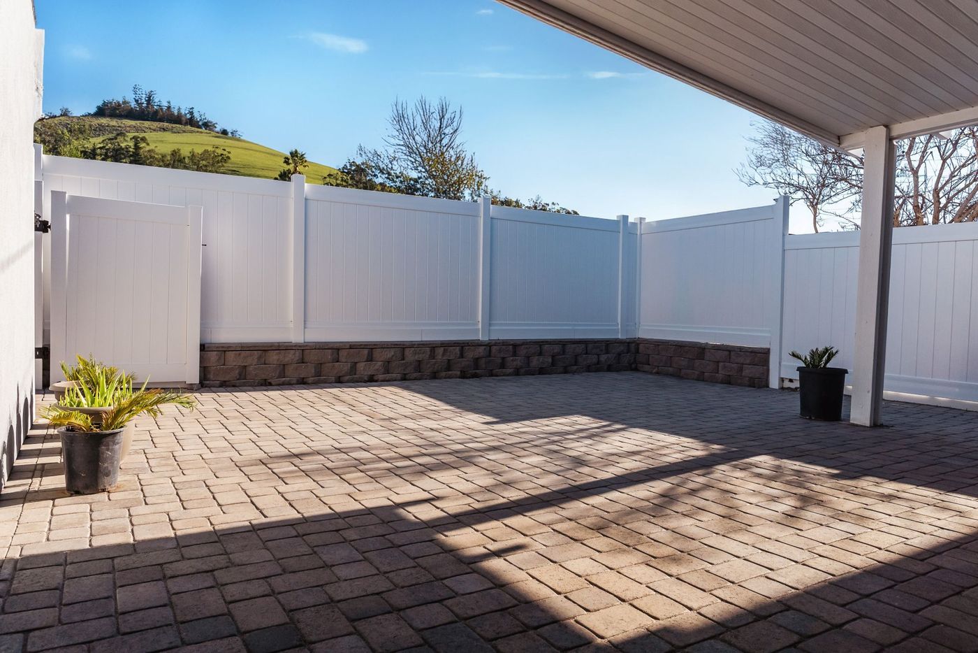 Interlocking paver driveway extending along the side yard of a Morro Bay home with white vinyl fencing.