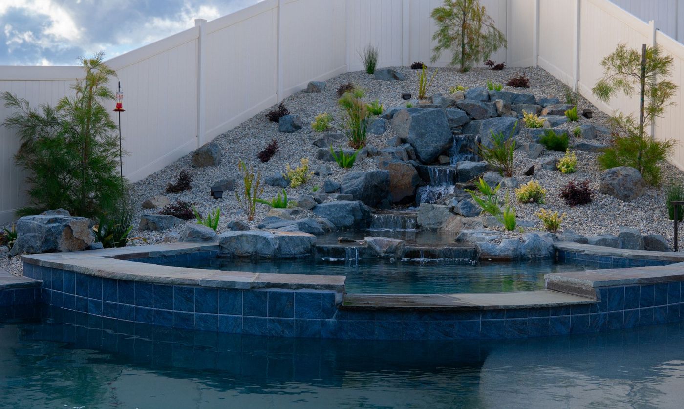 Close-up of raised spa edge with cascading natural stone waterfall flowing into a custom swimming pool surrounded by gravel landscaping