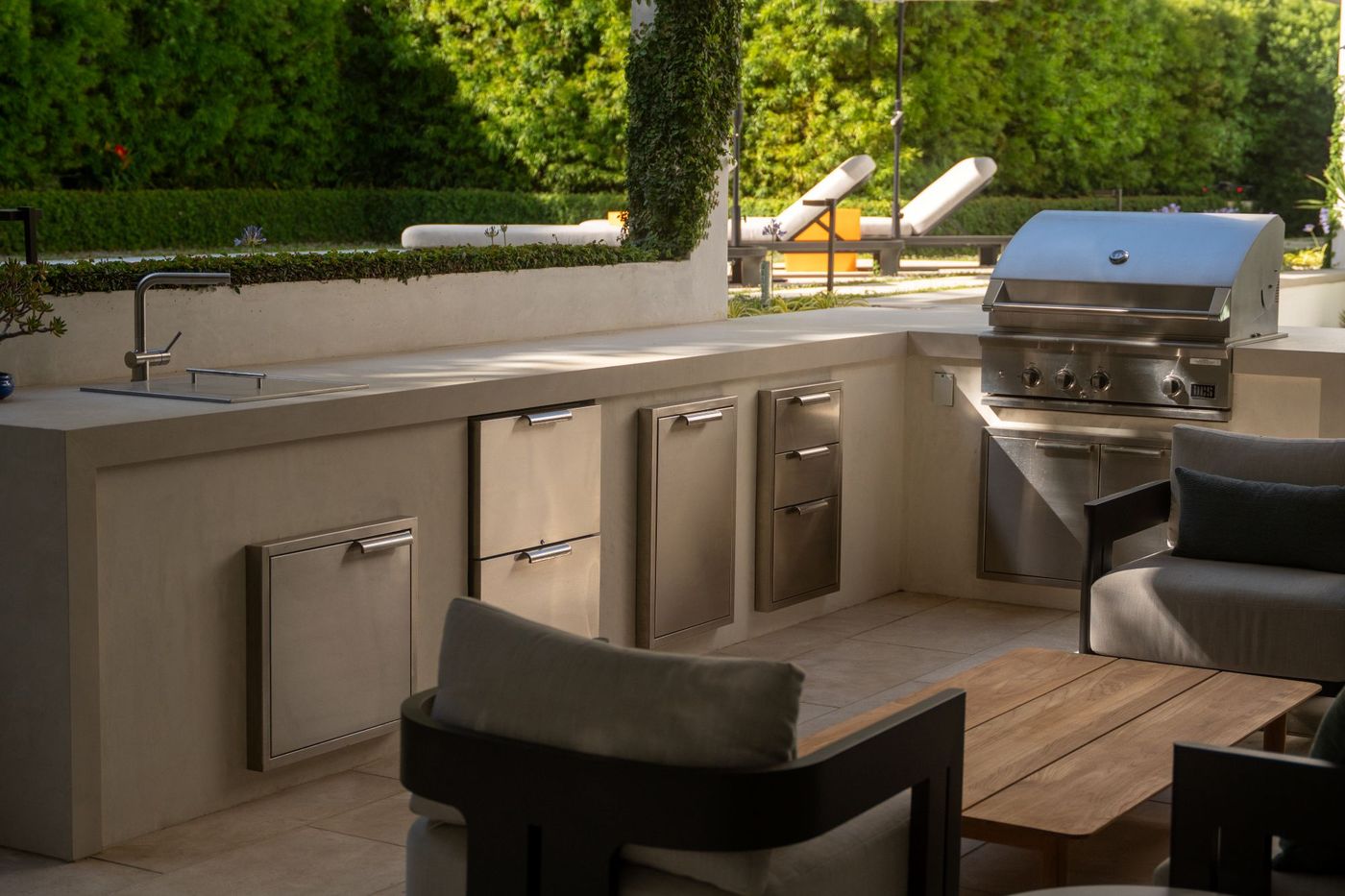 Custom outdoor kitchen featuring stainless steel grill, storage drawers, and countertop seating in a contemporary backyard