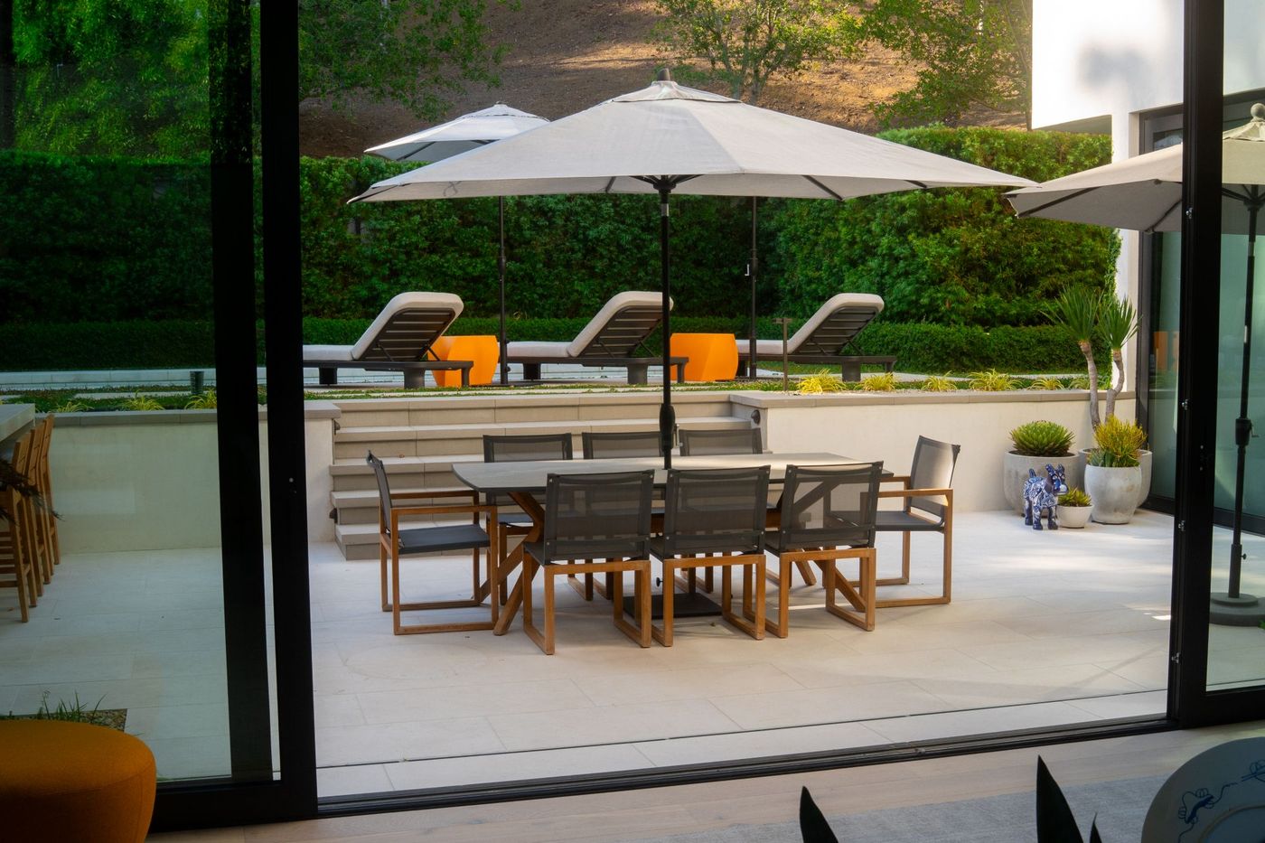View through sliding glass doors showing outdoor dining patio, steps, and pool lounge chairs in modern backyard.