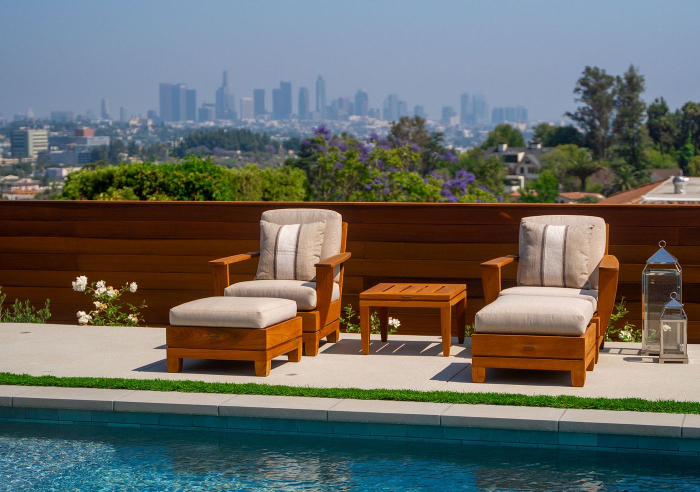 Outdoor lounge chairs and side table positioned beside a modern pool with distant Los Angeles skyline and hillside landscape in the background.