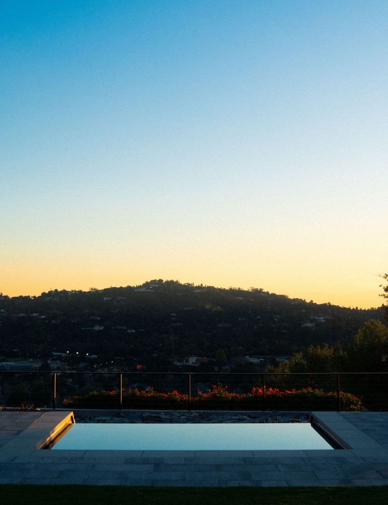 Reflective spa-edge pool at sunset with a hillside city view