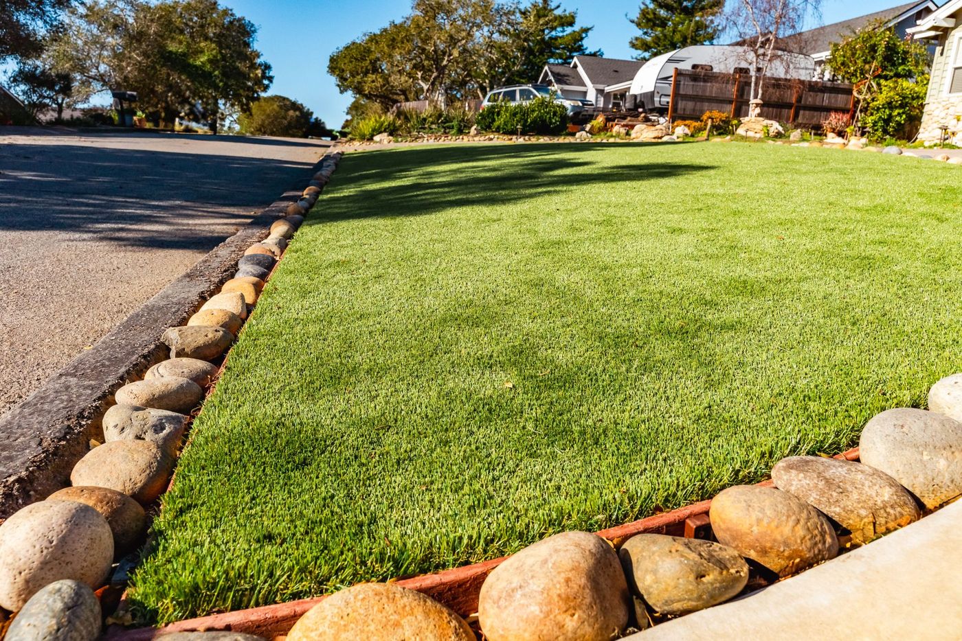 Artificial turf installation in a San Luis Obispo front yard with decorative river rock edging and clean curb transition.