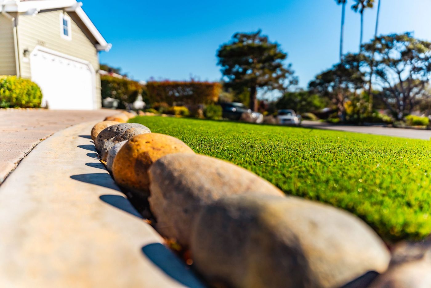 Close-up detail of artificial turf installation with decorative river rock border in a San Luis Obispo front yard.