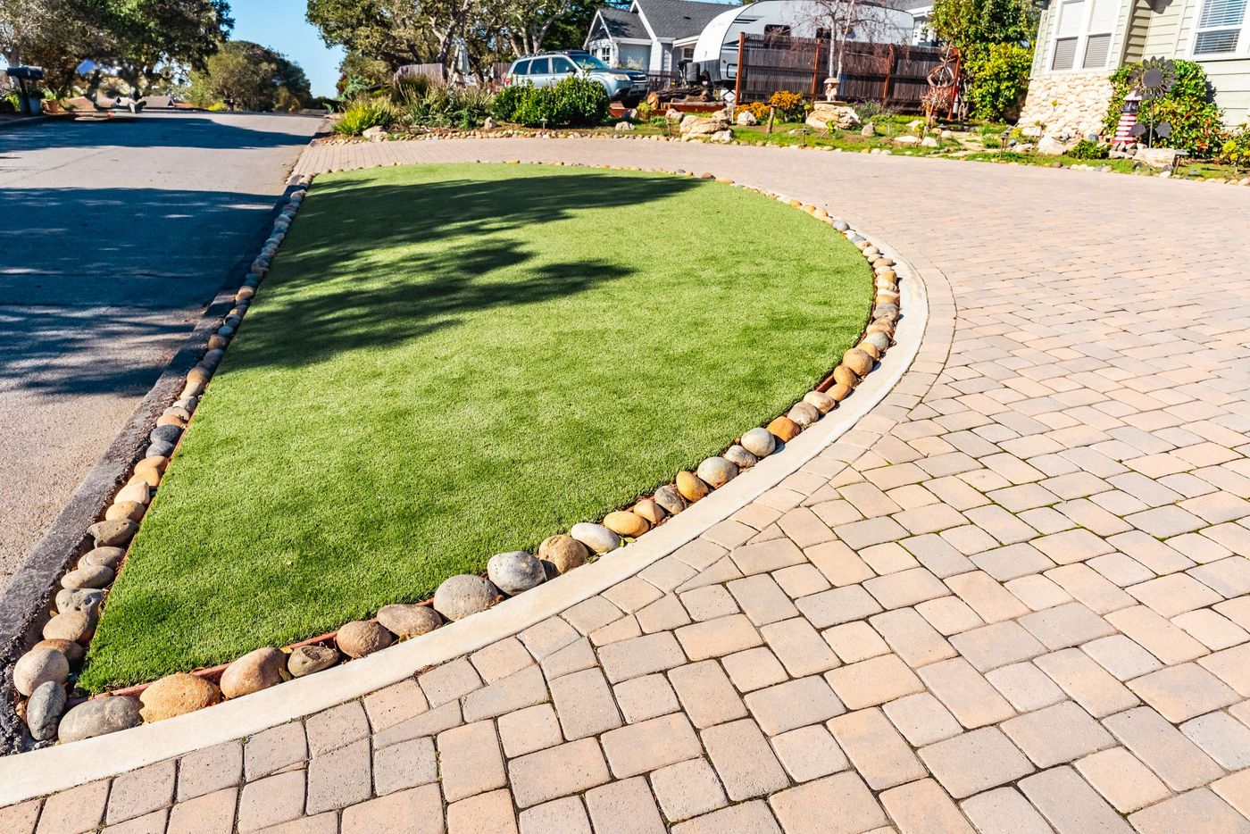 Curved artificial turf lawn in San Luis Obispo bordered by smooth river rocks and adjacent paver driveway.