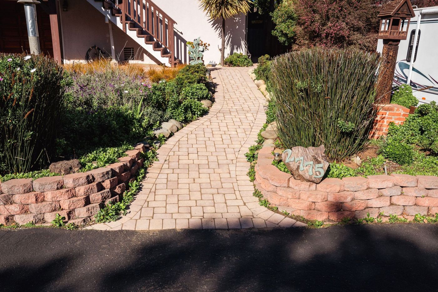 Curved paver garden pathway in San Luis Obispo bordered by decorative river rocks and landscaped shrubs.