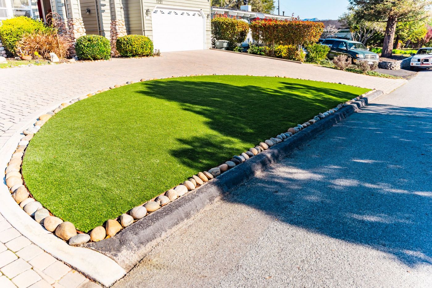San Luis Obispo front yard featuring synthetic grass lawn bordered by river rocks and a custom paver driveway.