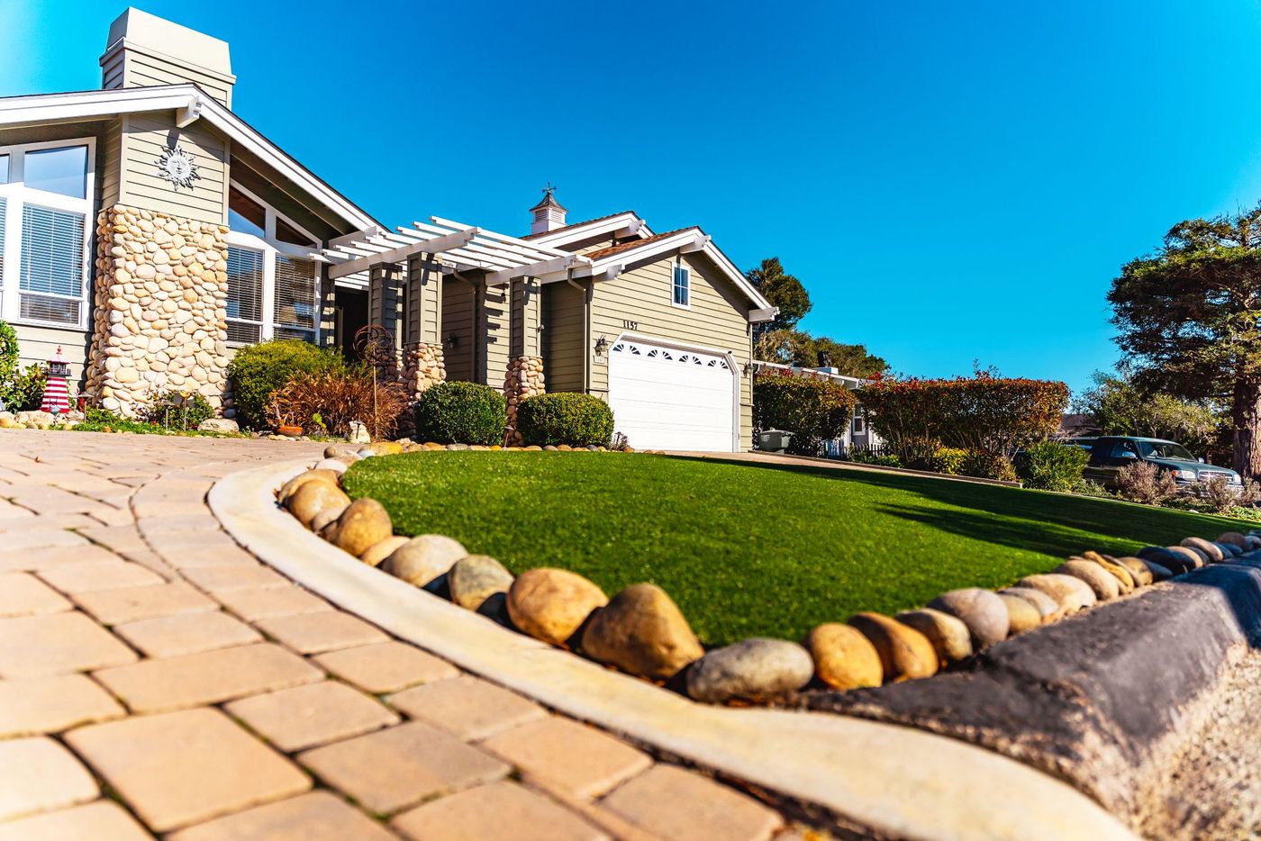 Front yard renovation in San Luis Obispo with synthetic turf lawn, decorative rock edging, and upgraded paver driveway.