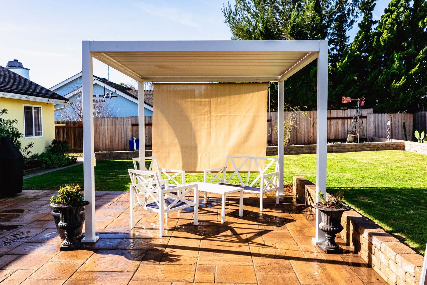 Spacious backyard patio and pergola installation in Santa Maria featuring textured pavers, lawn, and raised retaining walls.