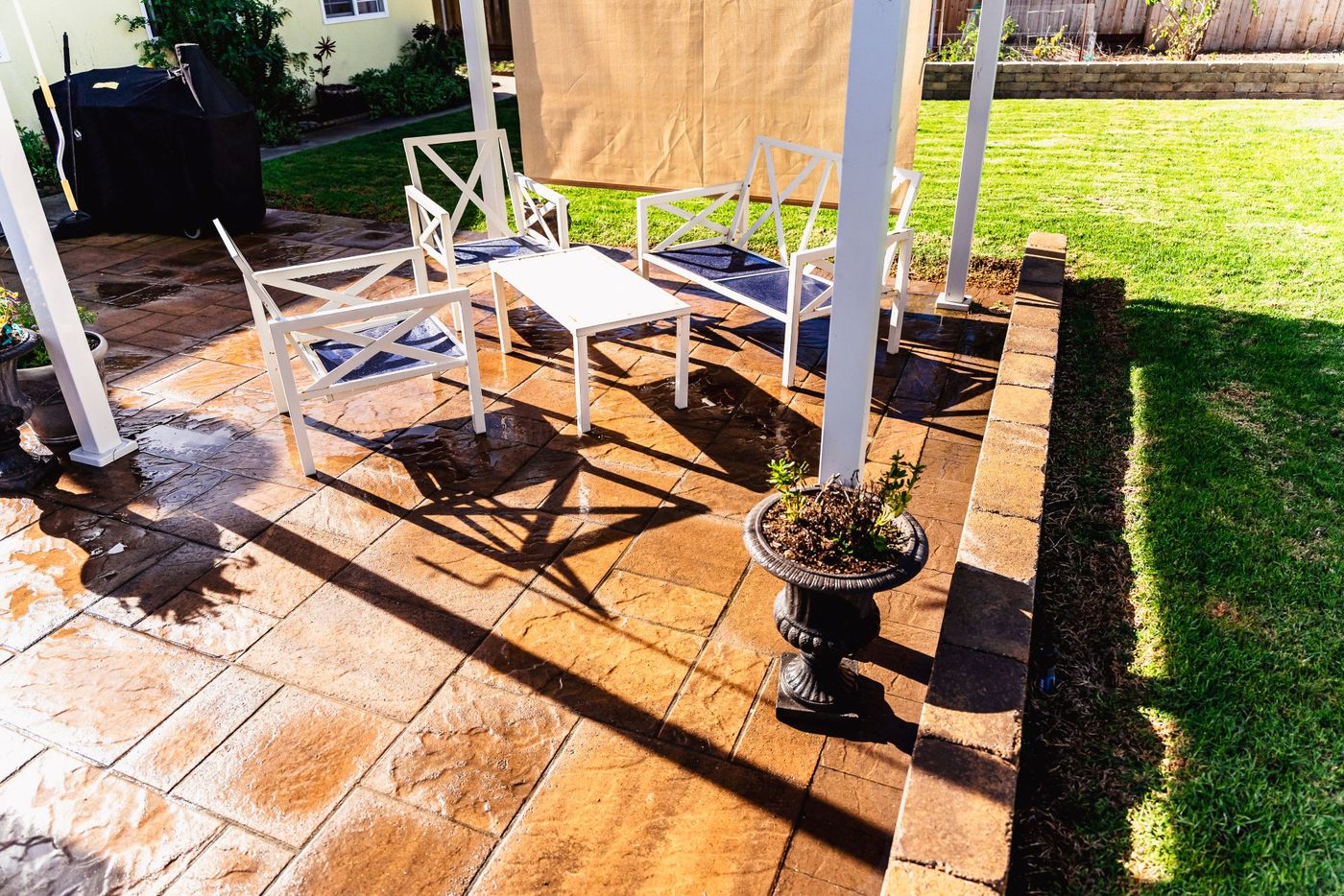 Outdoor seating arranged under a pergola on a textured paver patio in a Santa Maria backyard landscape design.