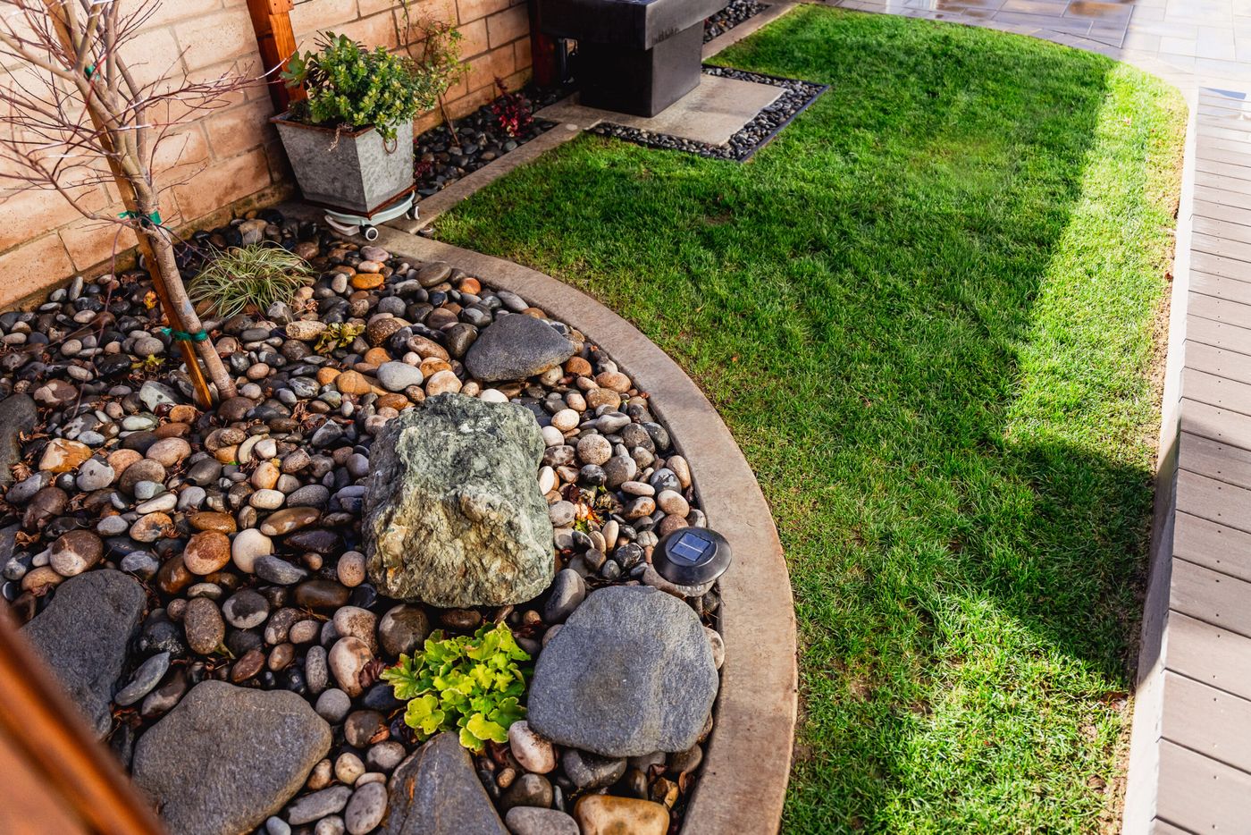 Decorative river rock planting bed with curved concrete edging in a Santa Maria side yard.