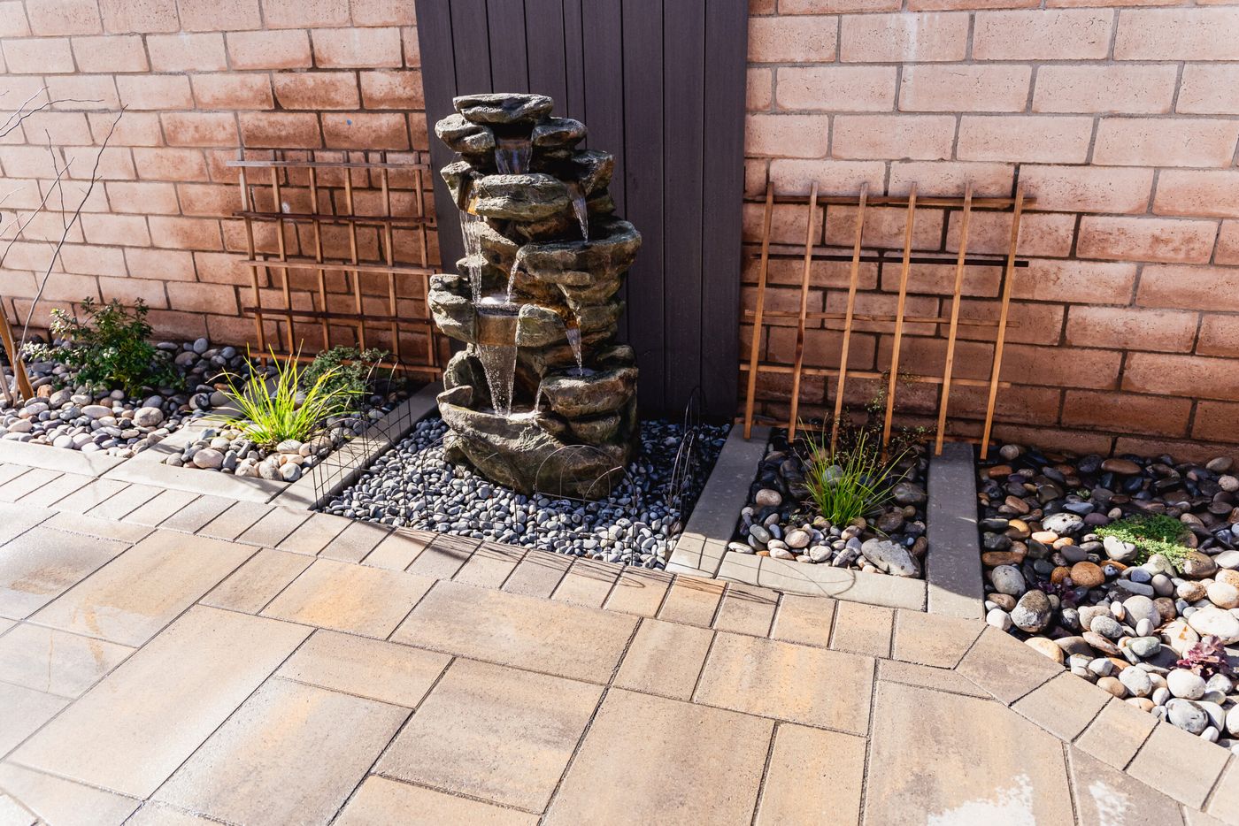 Stacked stone waterfall fountain surrounded by river rock and pavers in Santa Maria.