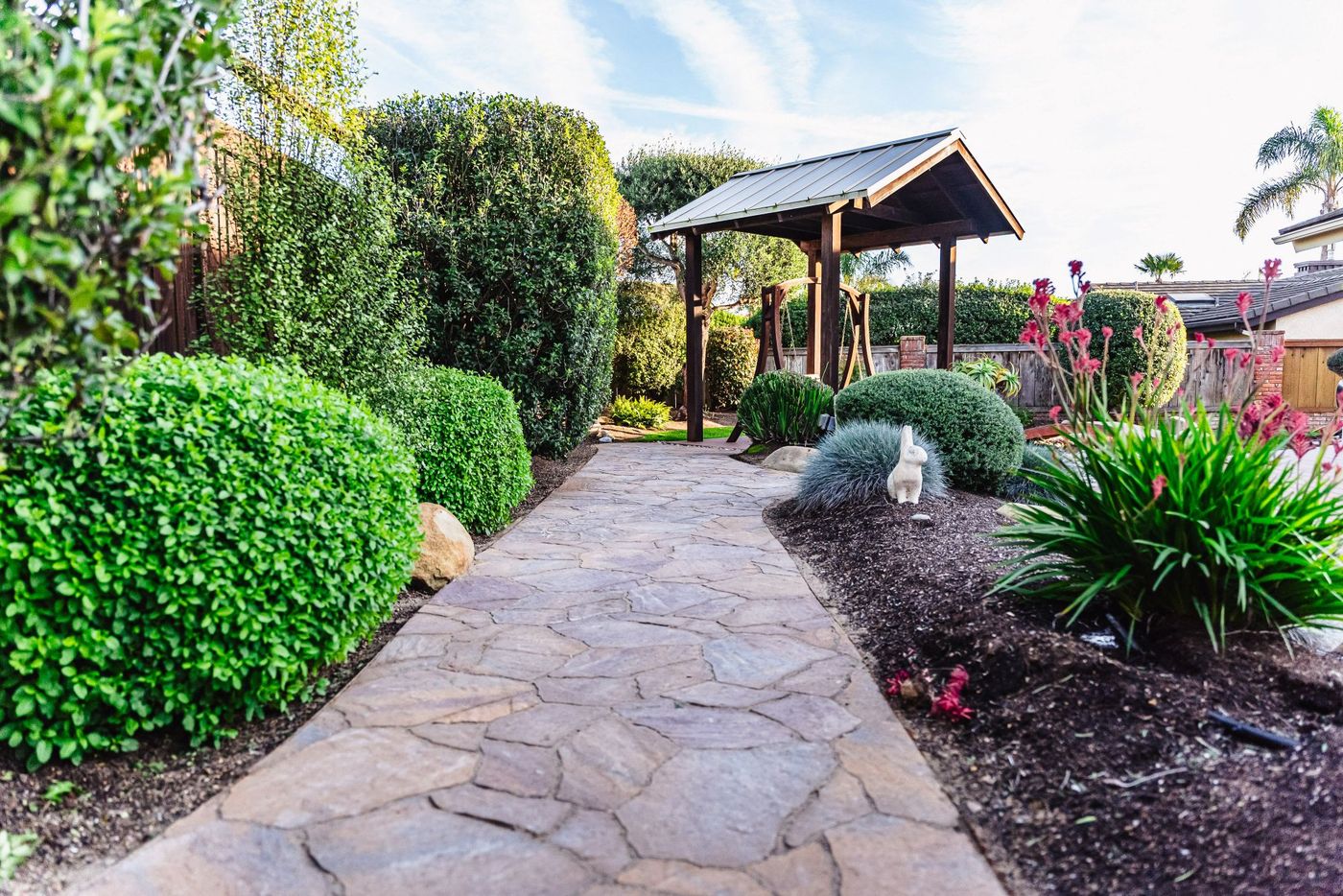 Curved stamped concrete garden walkway leading through landscaped beds toward a wooden pergola in Shell Beach.