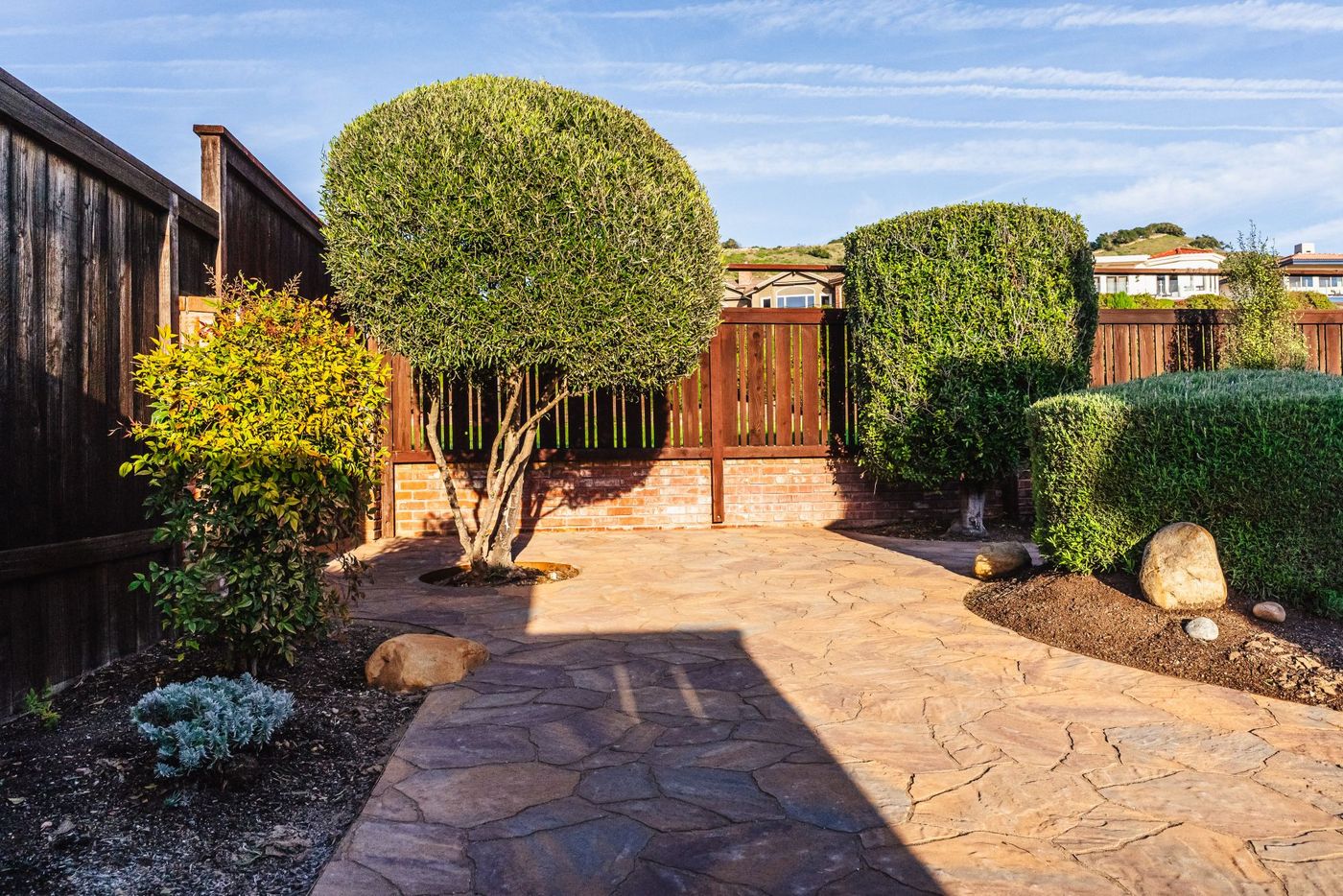 Stamped concrete courtyard with trimmed ornamental trees and brick fencing in a Shell Beach residence.